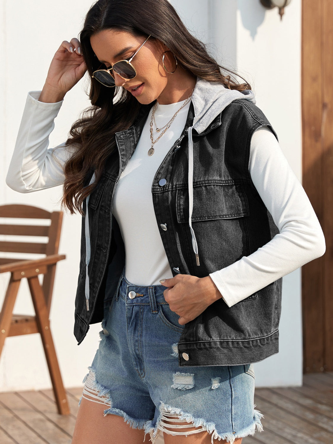 Woman wearing sleeveless denim jacket with drawstrings and button front.