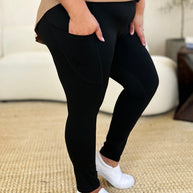 Black wide waistband sports leggings with a basic style, stretchy nylon-spandex material, and side pockets, shown paired with white sneakers.