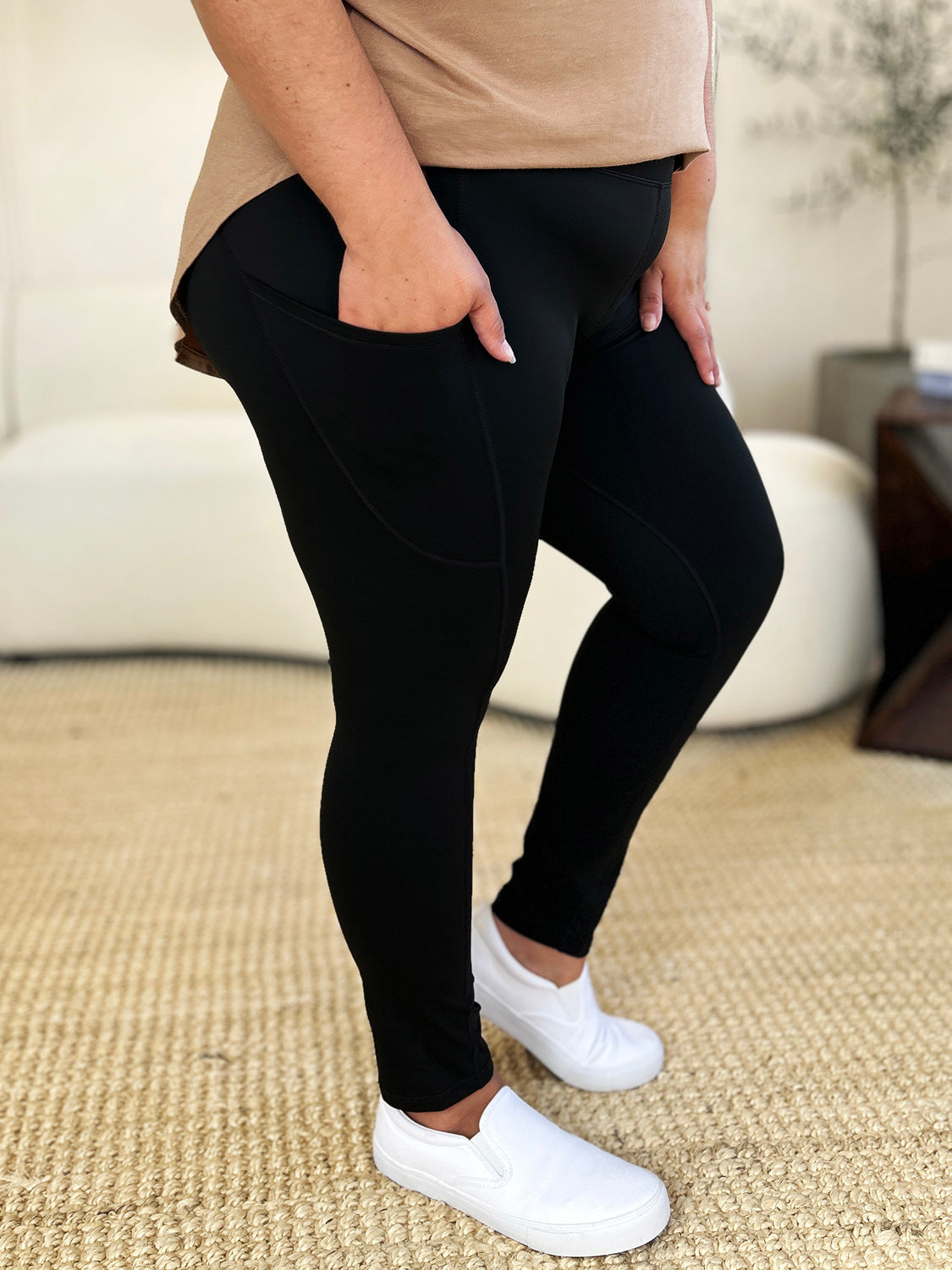 Black wide waistband sports leggings with a basic style, stretchy nylon-spandex material, and side pockets, shown paired with white sneakers.