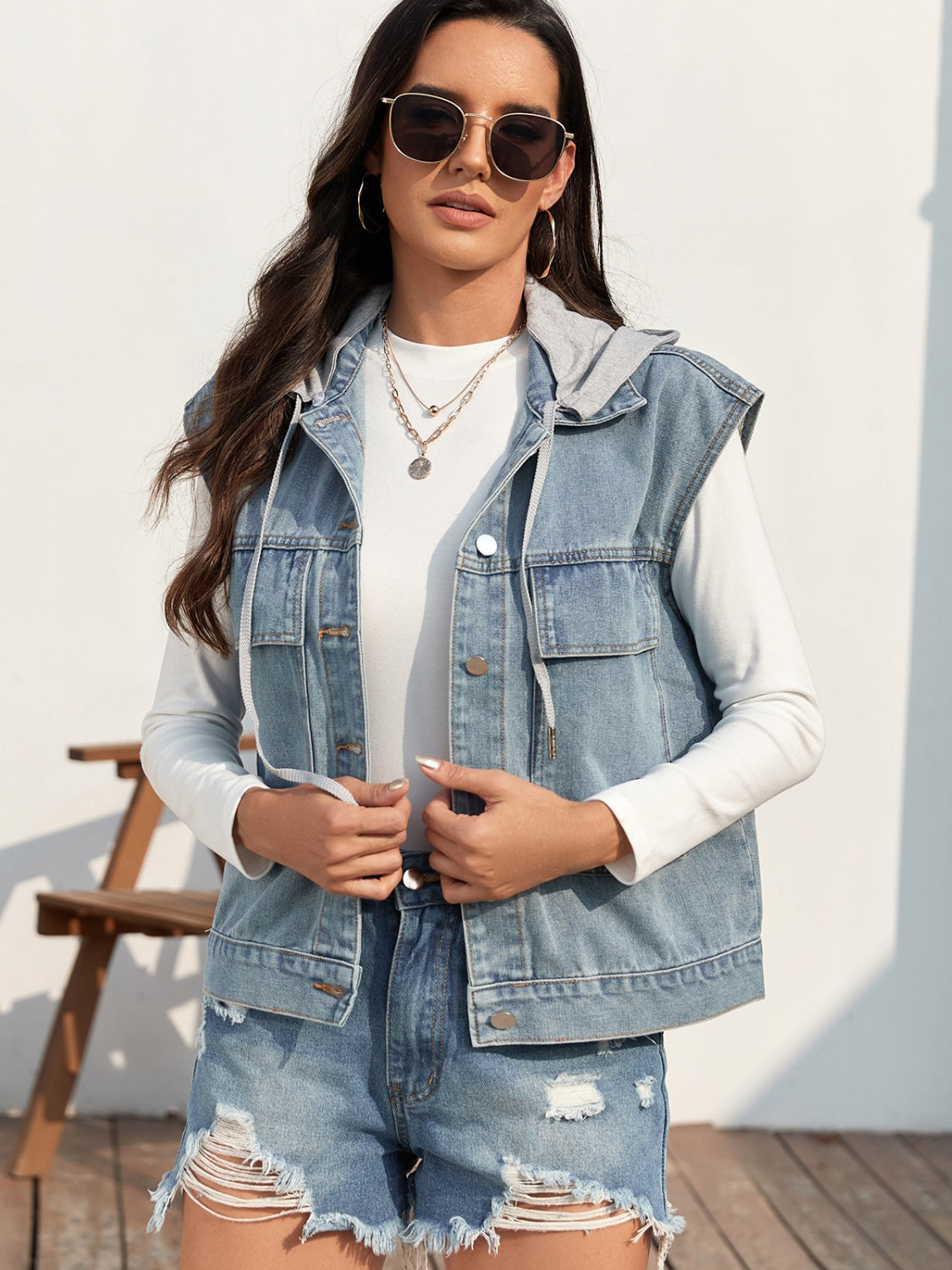 Sleeveless denim jacket with button-up front and drawstring, worn by a model with sunglasses.