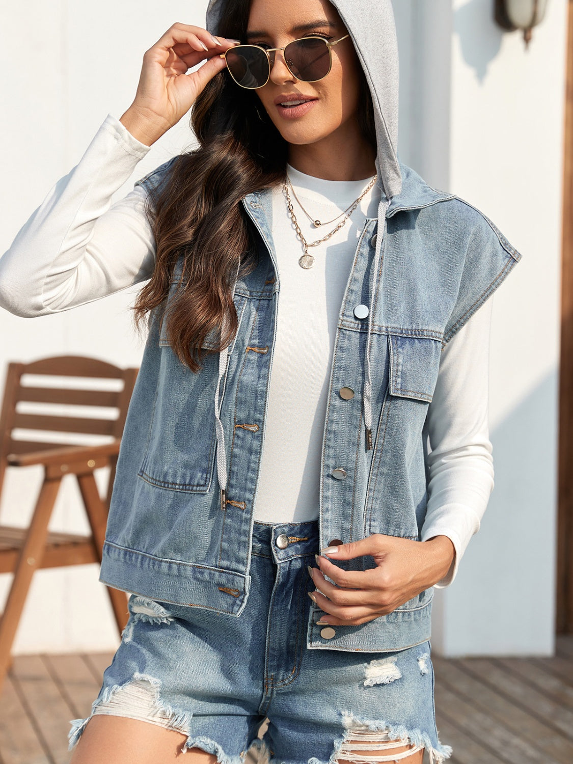 Sleeveless denim jacket with drawstring and button-up design worn by model outdoors.