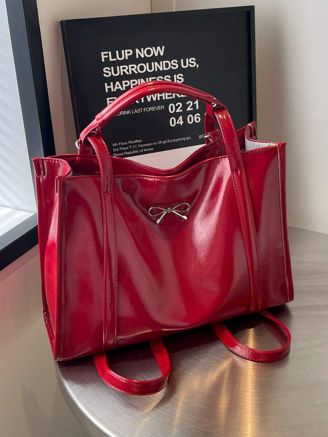 Red PU leather bow shoulder bag on table, spacious design.