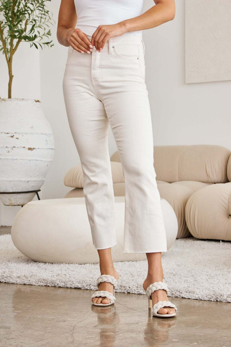 RFM Mini Mia high waist raw hem jeans with tummy control, shown in white, styled in a modern living room.