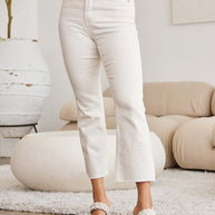 RFM Mini Mia high waist raw hem jeans with tummy control, shown in white, styled in a modern living room.