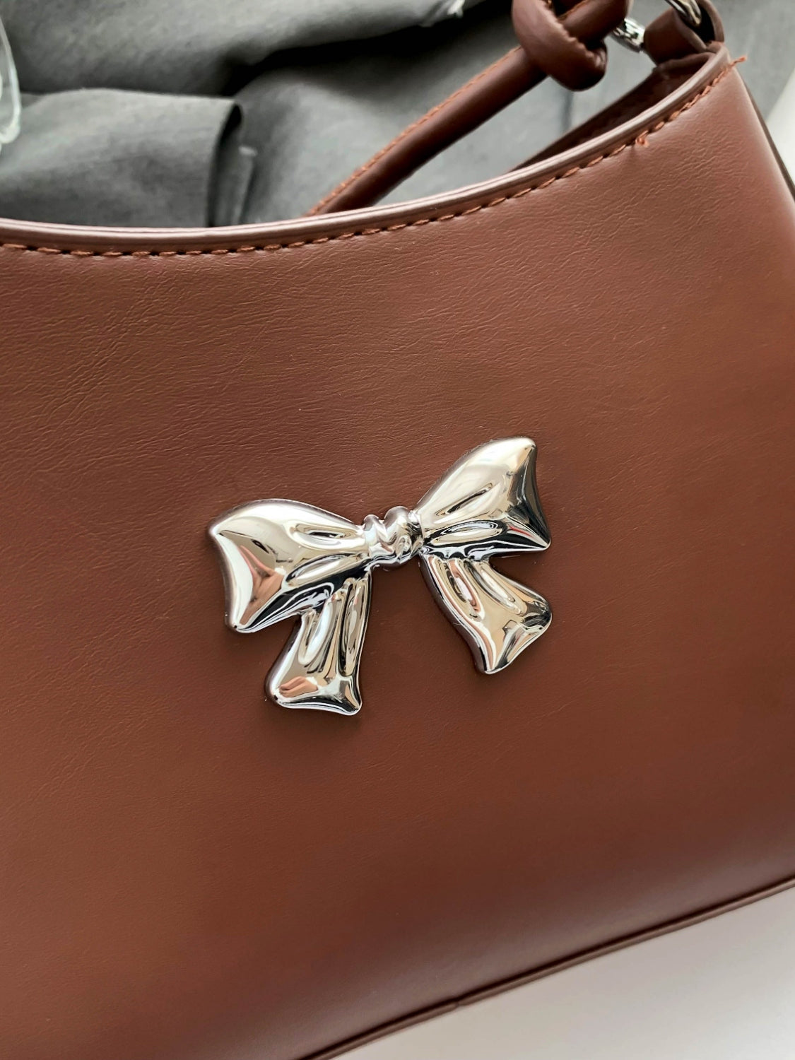 Small PU leather handbag with knotted strap and bow detail.