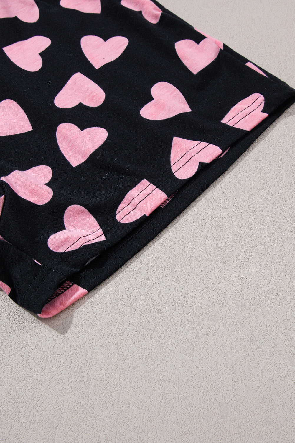 Heart print long sleeve top fabric detail with pink hearts on black background.