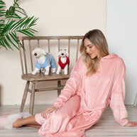 Full size pocketed hooded midi lounge dress in pink worn by a woman sitting on a floor with plush dog toys on a chair in the background.