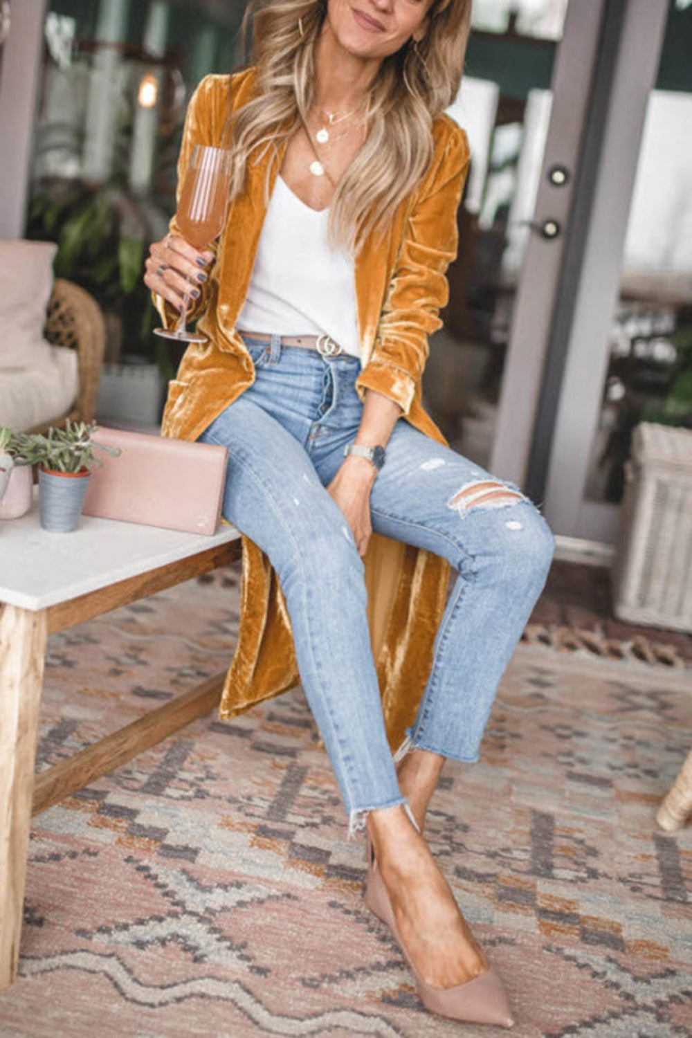 Open front long sleeve coat in mustard yellow with a slit detail, paired with jeans and a white top, held by a woman seated indoors.