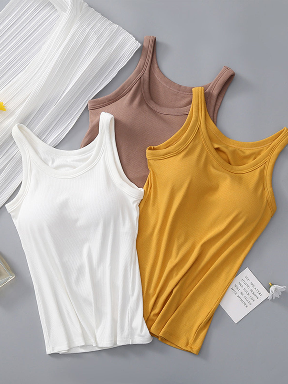 Round neck tank with built-in bra in white, brown, and mustard colors displayed on a flat surface.