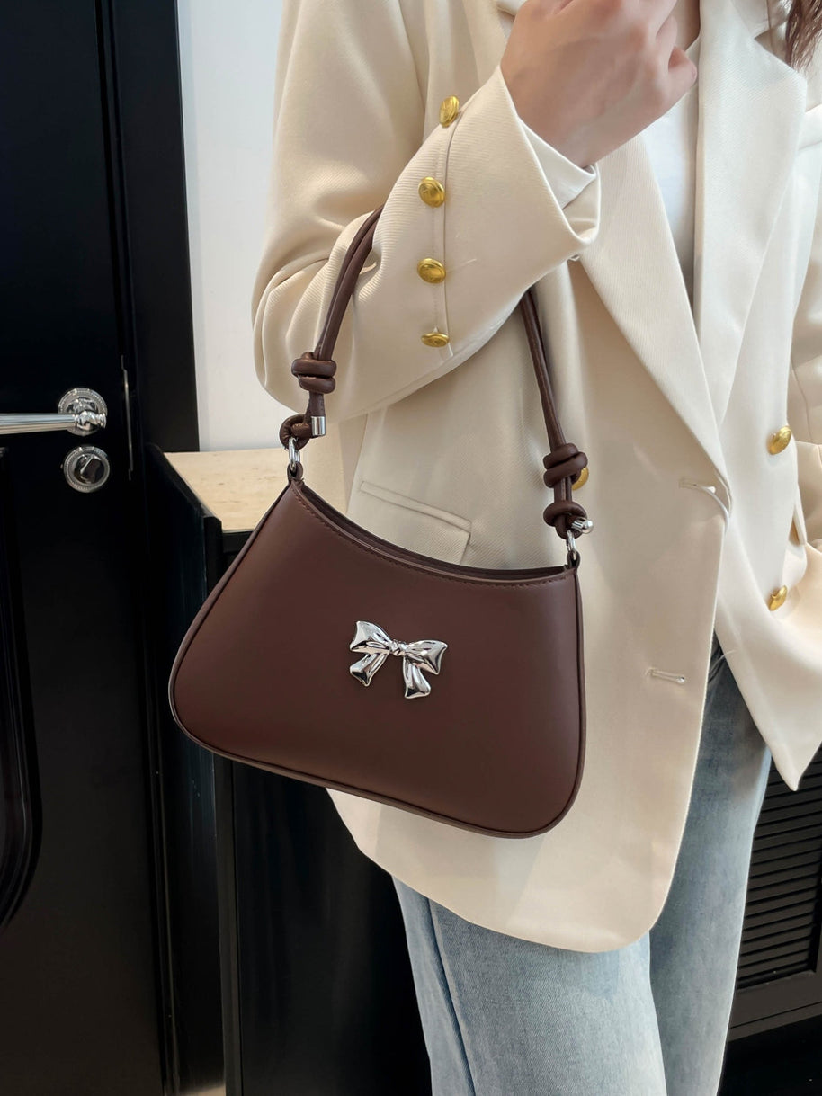 Small bow PU leather knotted strap handbag in brown displayed on shoulder.