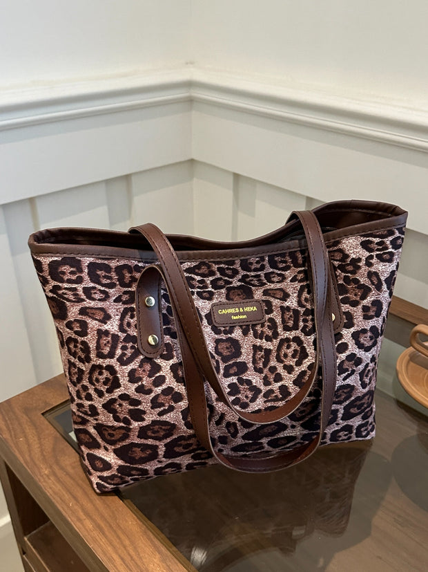 Leopard polyester tote bag with large size and brown handles on a table.