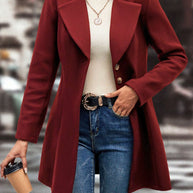 Woman wearing red collared neck button-up long sleeve coat with jeans, holding coffee cup.