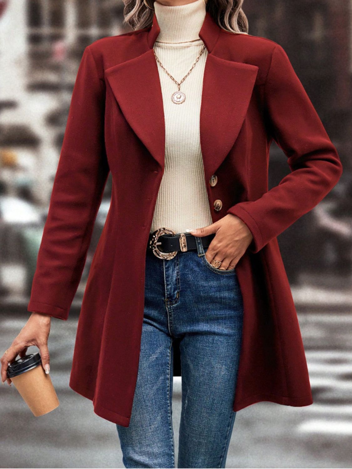 Woman wearing red collared neck button-up long sleeve coat with jeans, holding coffee cup.