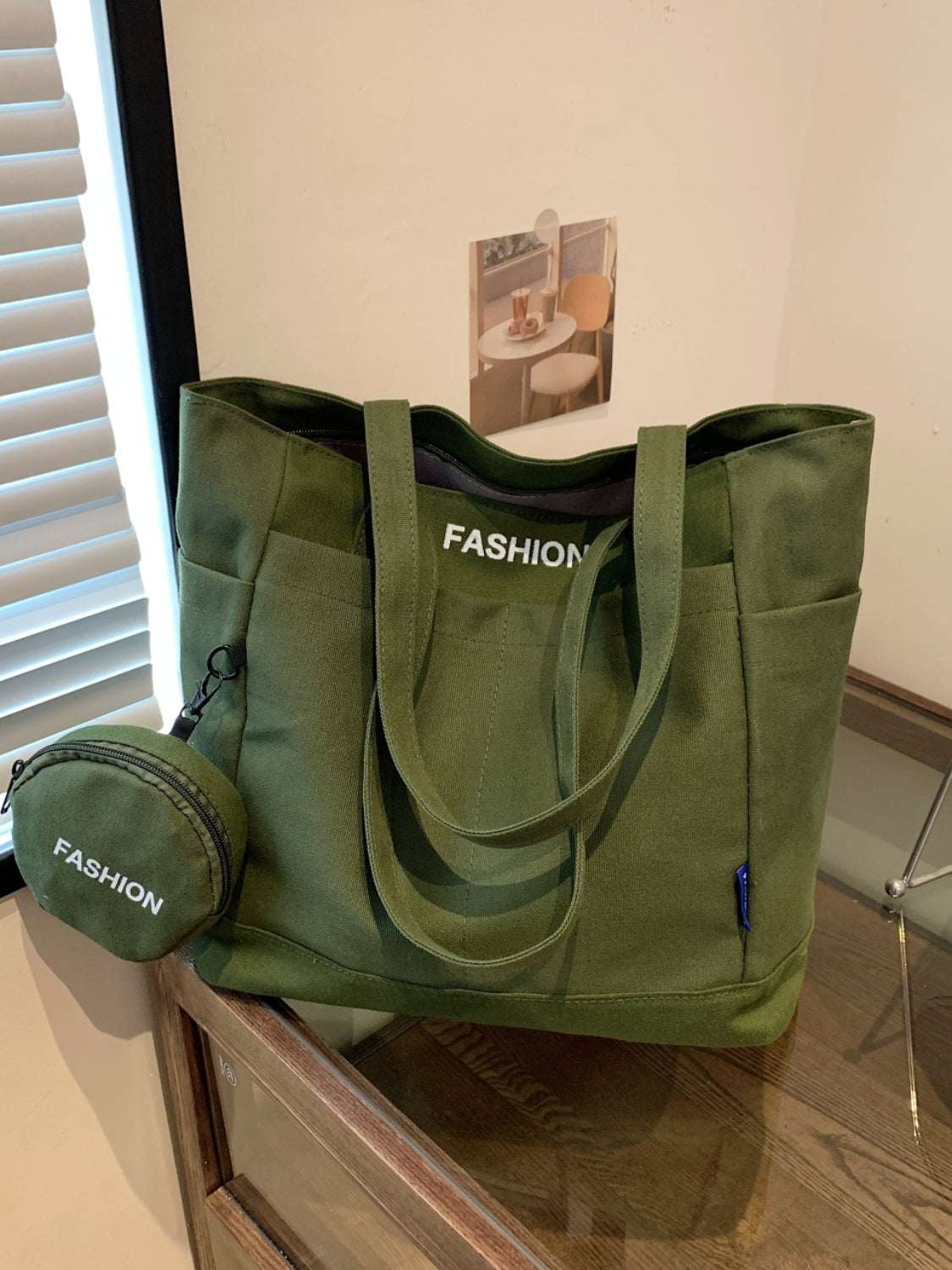 Green canvas tote bag with pouch on a table, featuring "Fashion" text on both items.