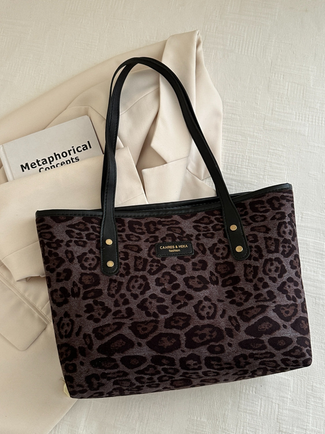 Leopard polyester tote bag on a white surface with black handles.