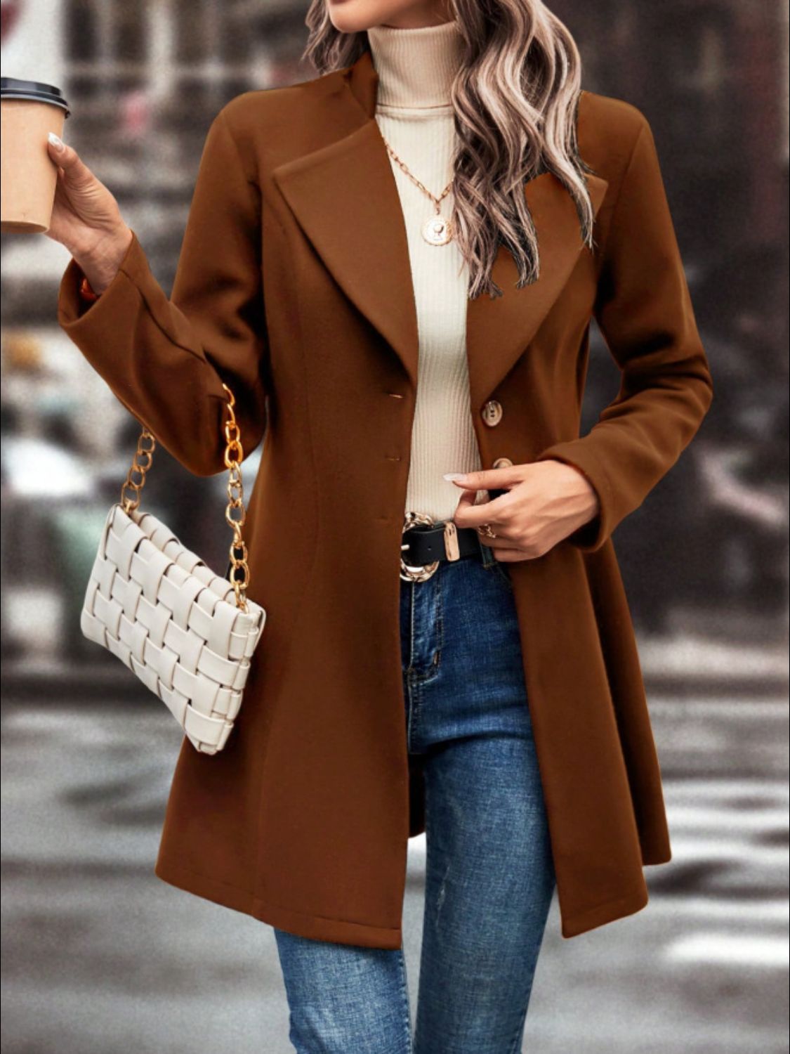 Stylish collared neck button-up long sleeve coat in brown worn over a cream turtleneck sweater with jeans, accessorized with a white woven handbag.