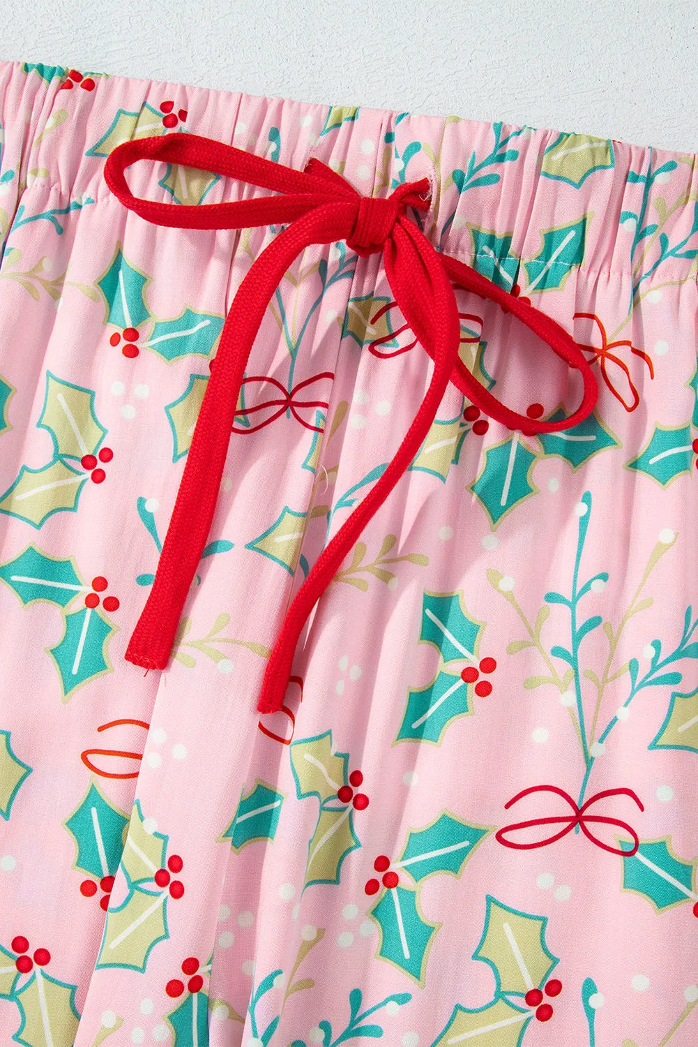 Pink lounge pants with printed festive holly design and red drawstring tie.