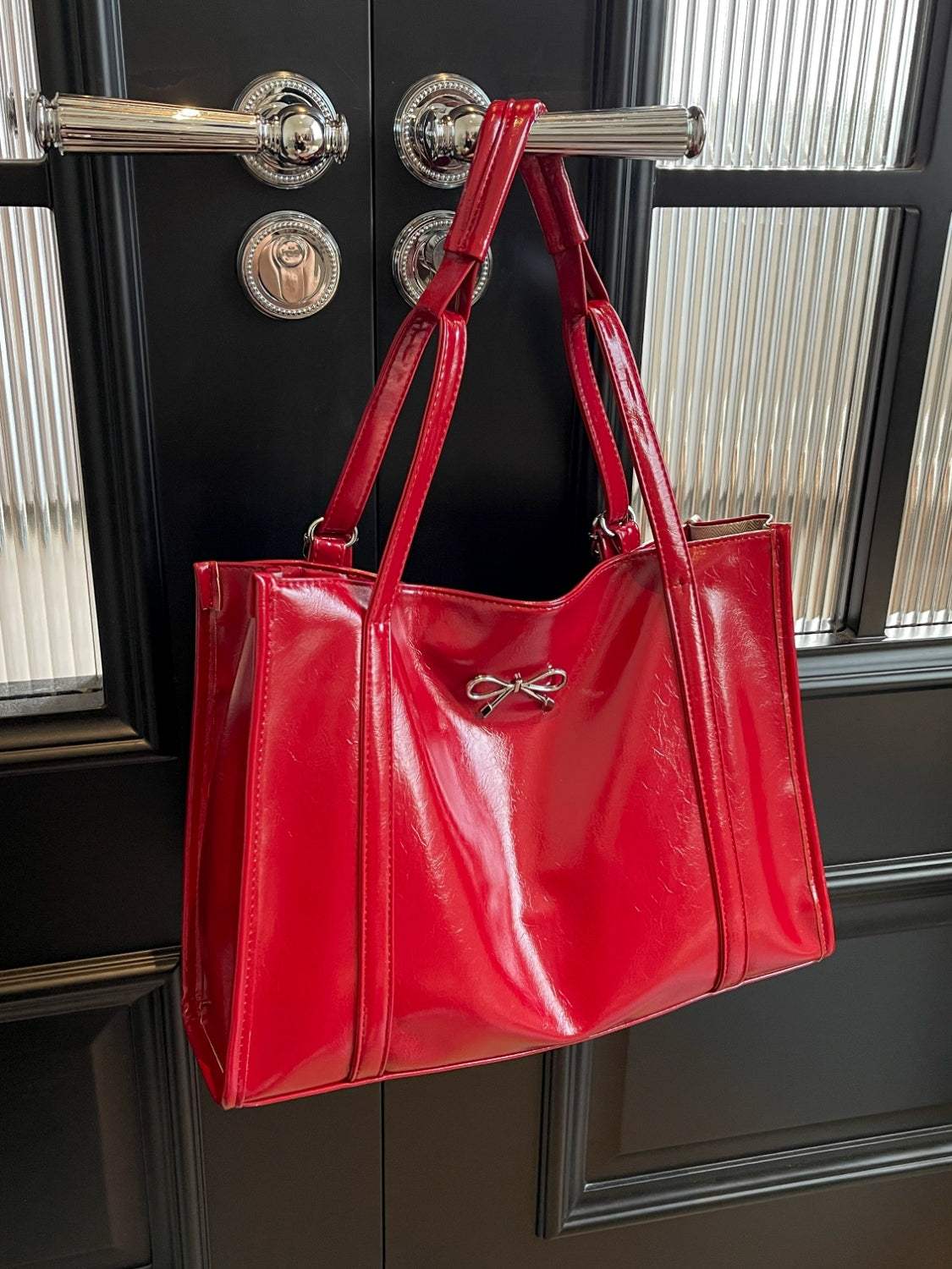 Red PU leather bow shoulder bag hanging on a door handle.