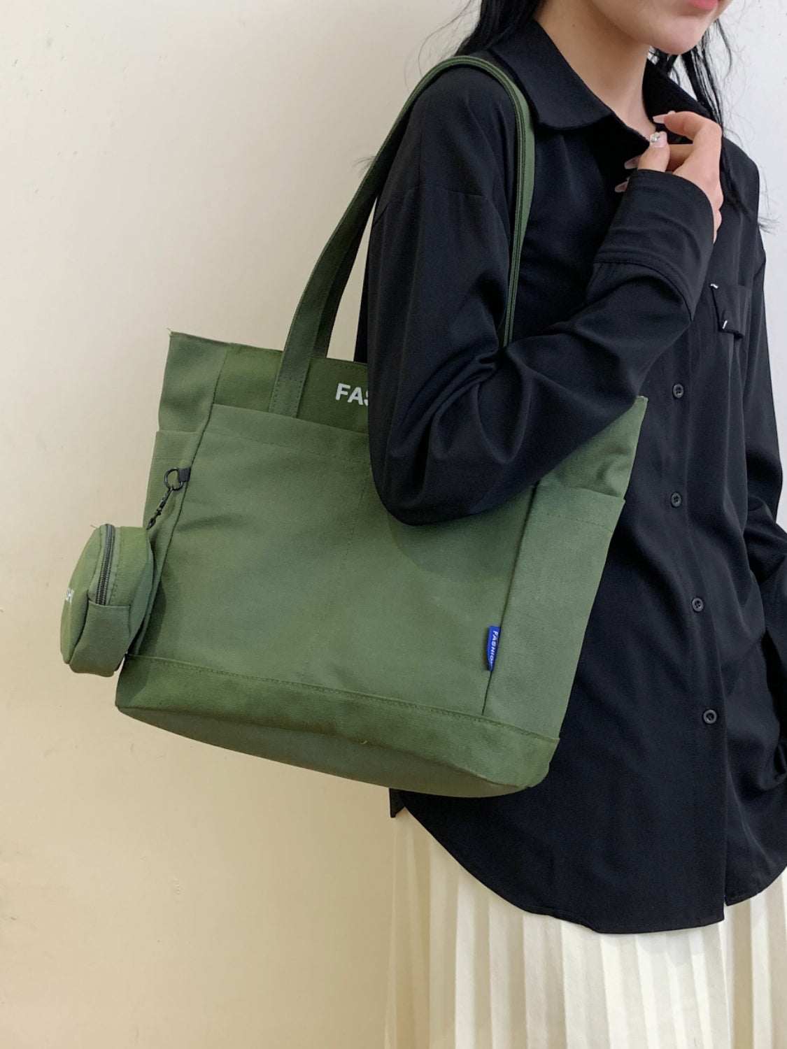 Green canvas tote bag with pouch, durable and spacious, styled with a black outfit.