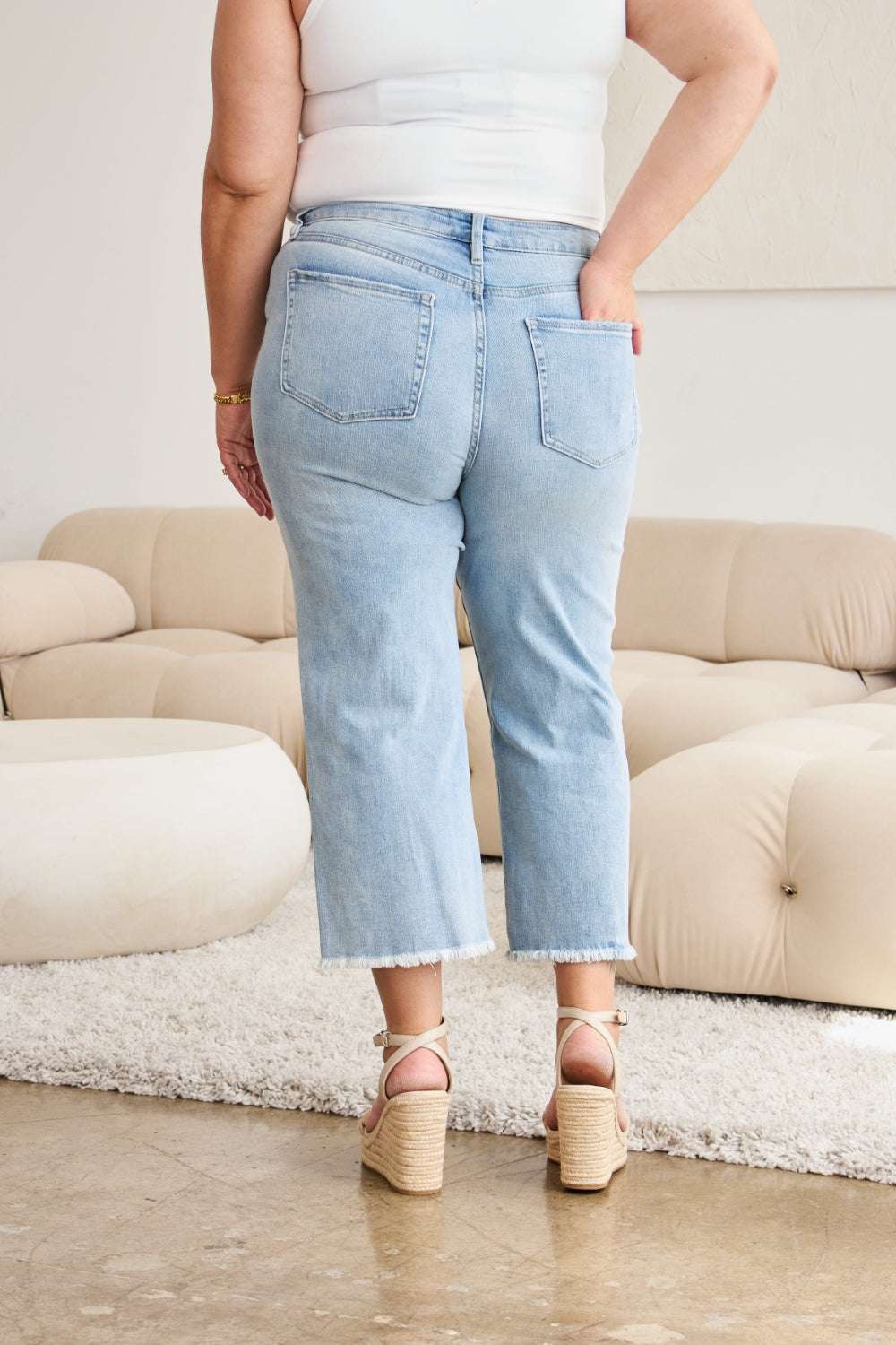 RFM Full Size Tummy Control High Waist Raw Hem Distressed Jeans on a model in a living room setting.